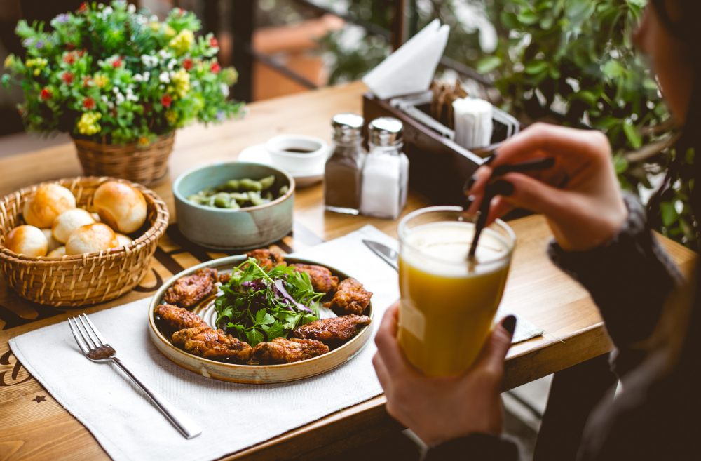 A person sitting at a table with a plate of chicken wings, a salad, and a glass of orange juice.
