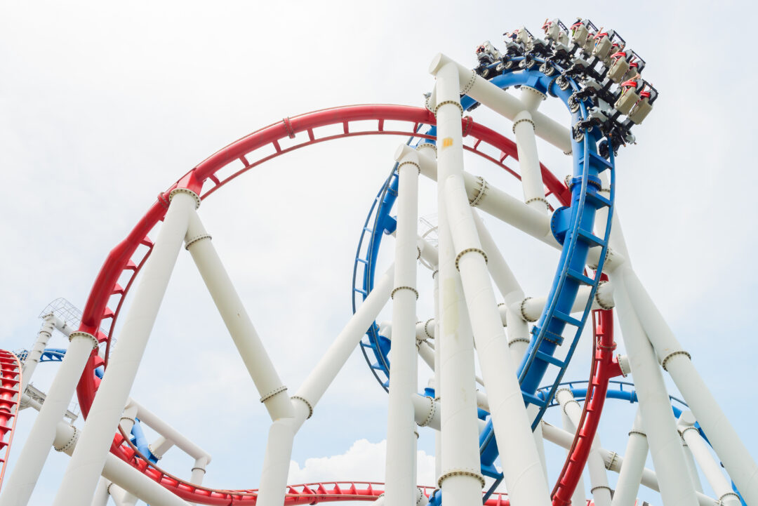 A roller coaster rail at a theme park, featuring steep curves and a thrilling atmosphere. The scene captures the excitement of the ride against a clear sky backdrop.